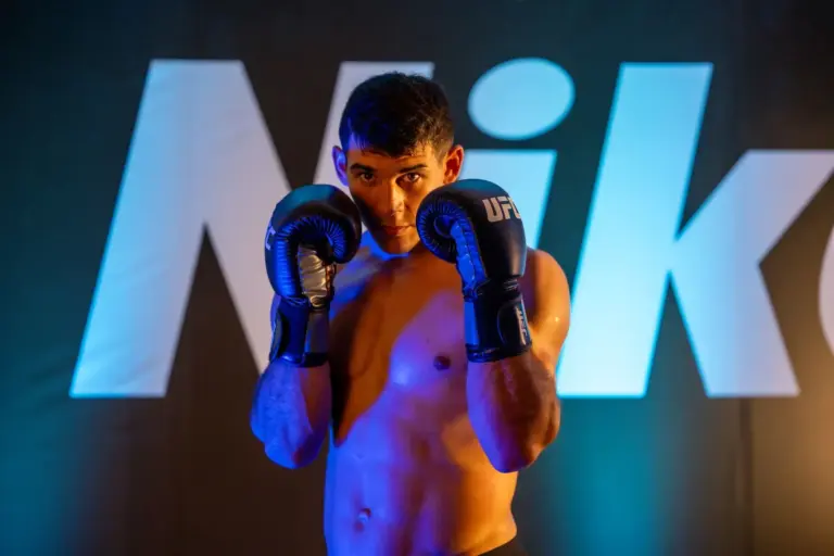 Gregory Rodrigues posing in a fighting stance wearing blue UFC gloves against a branded backdrop