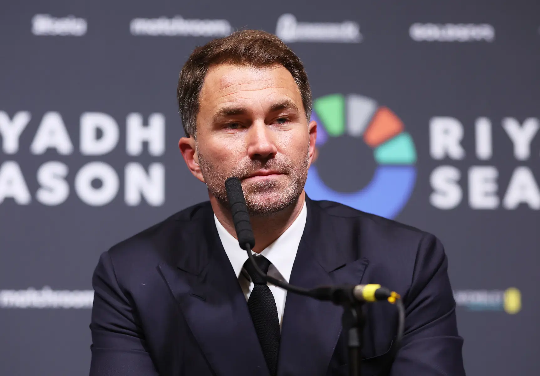 Eddie Hearn in een donkerblauw pak tijdens een persconferentie.